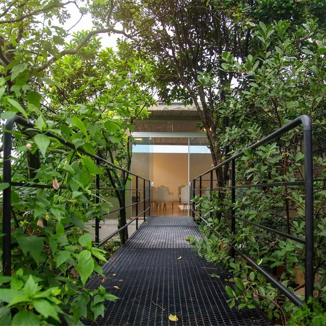 Passarela de entrada da EcoCasa, cercada de árvores, levando à sala envidraçada