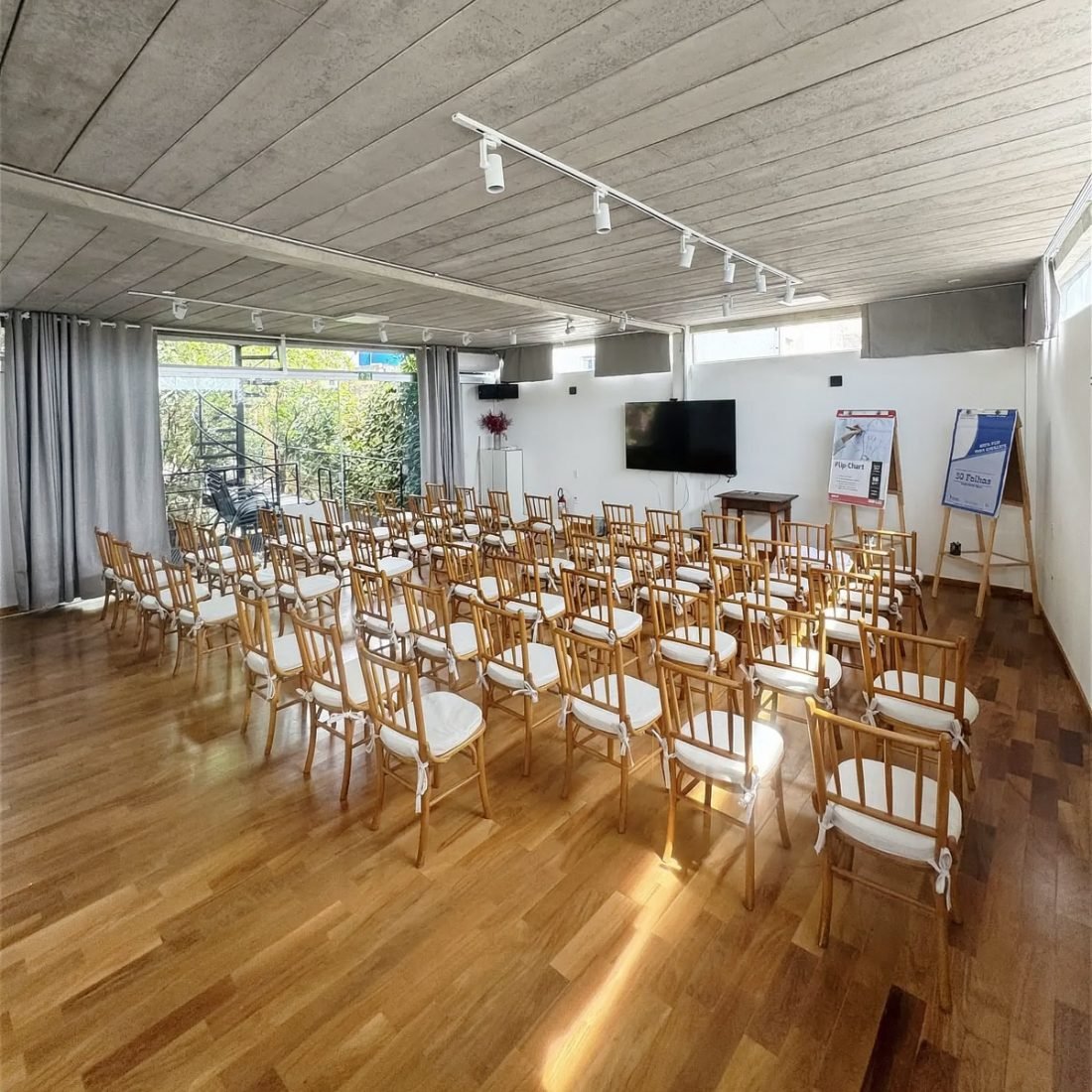 Sala principal da EcoCasa, com cadeiras de madeira, teto de concreto e janelas para o jardim